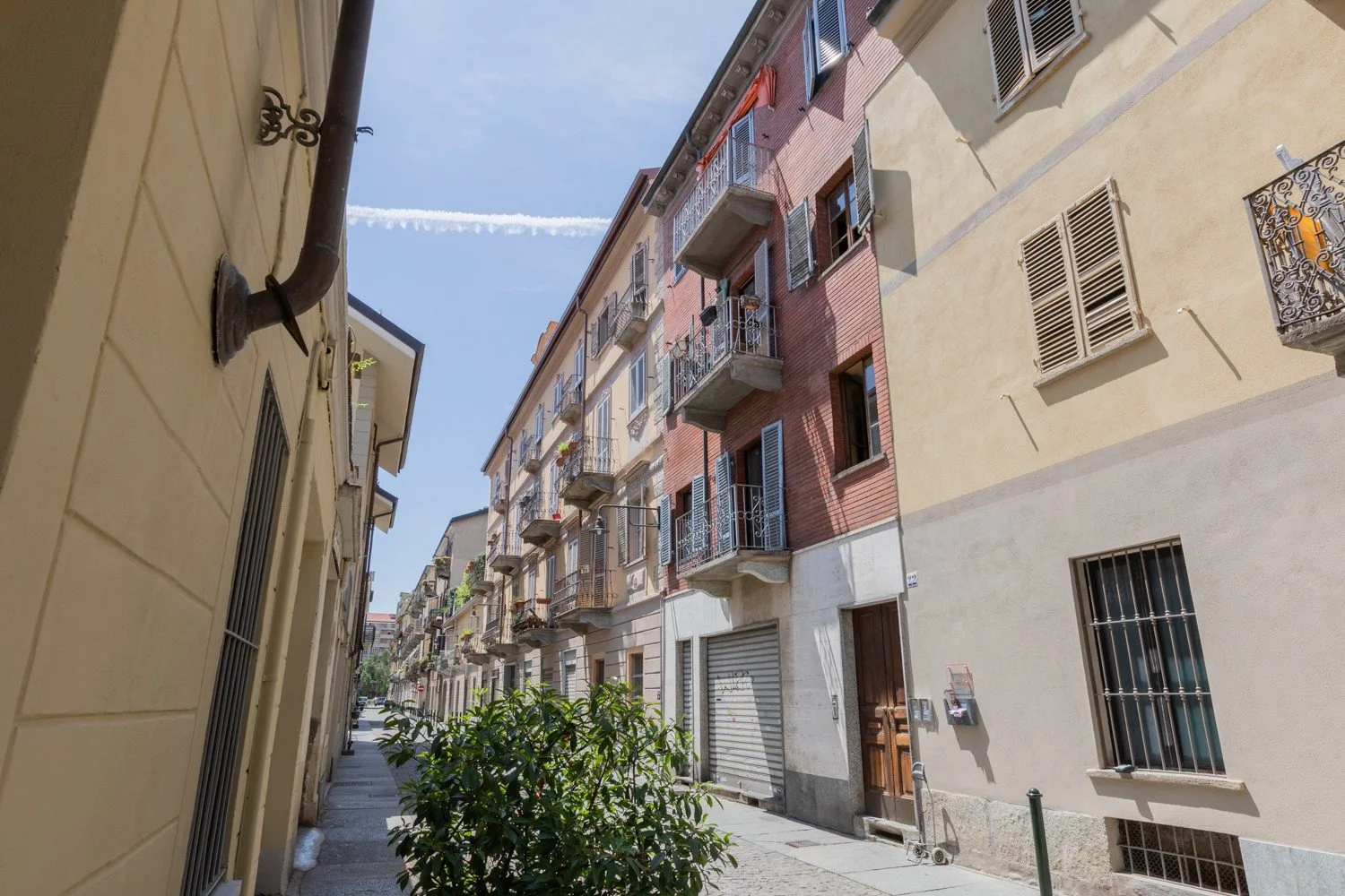 A narrow urban street runs between apartment buildings with balconies and ground-floor shops.