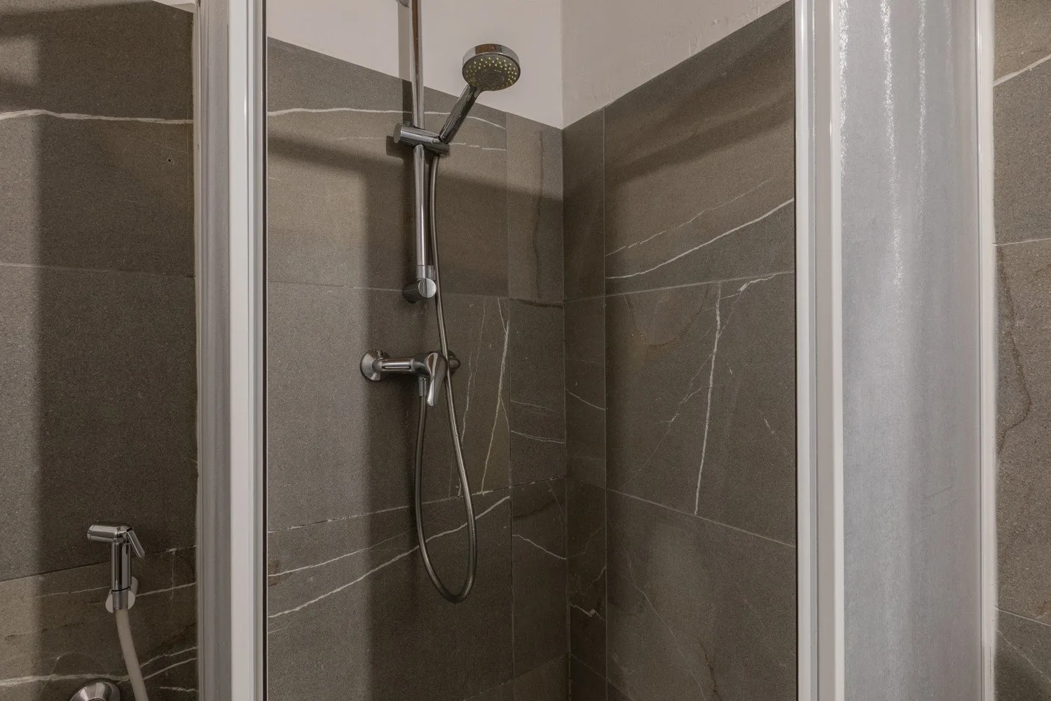 A tiled shower with a handheld showerhead and metal fixtures.