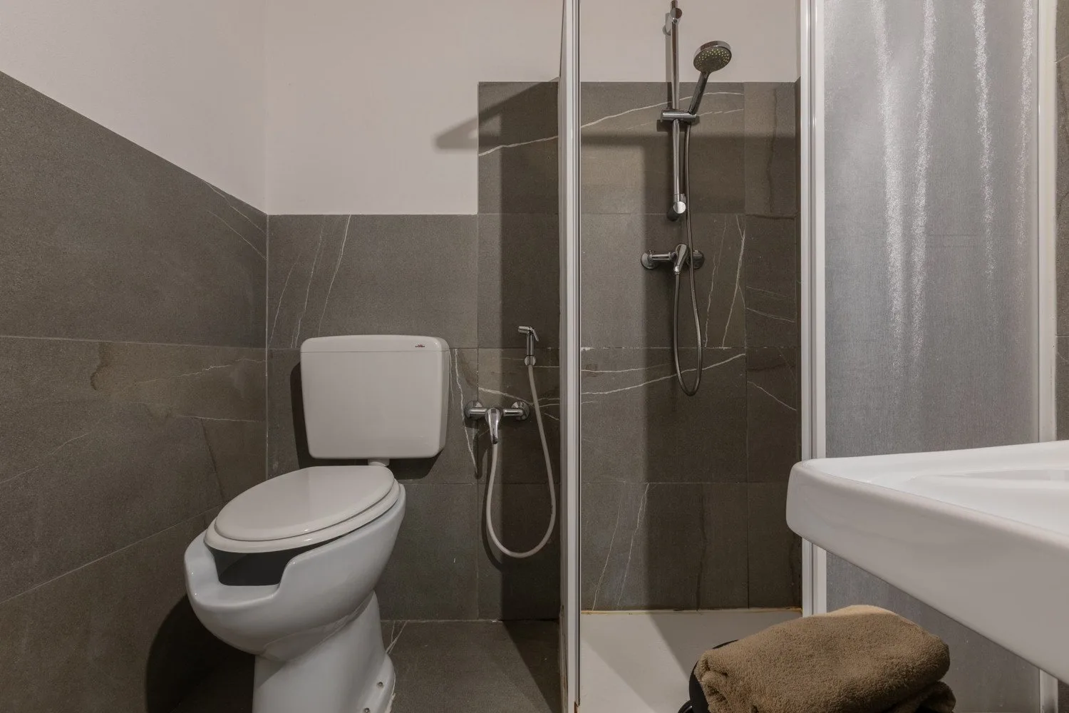 A tiled bathroom with a toilet, shower, and sink.