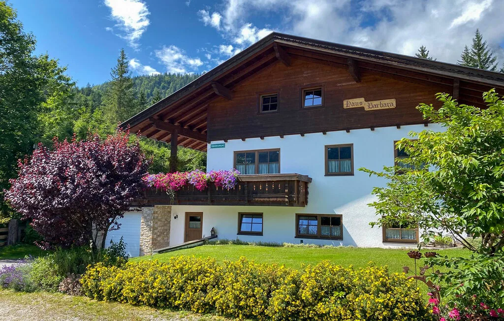 Una casa de estilo chalet está rodeada de arbustos floridos y colinas verdes.