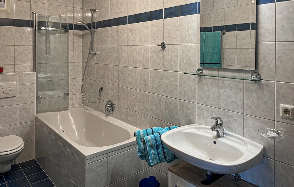 Un baño alicatado con bañera, lavabo y espejo de pared.