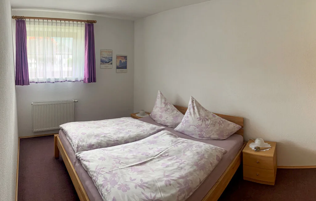 Un dormitorio con dos camas vestidas con ropa de cama floral clara junto a una ventana con cortinas.