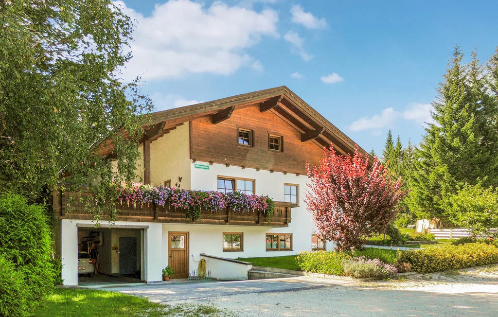 Una casa de estilo chalet está entre árboles, con flores en su balcón.