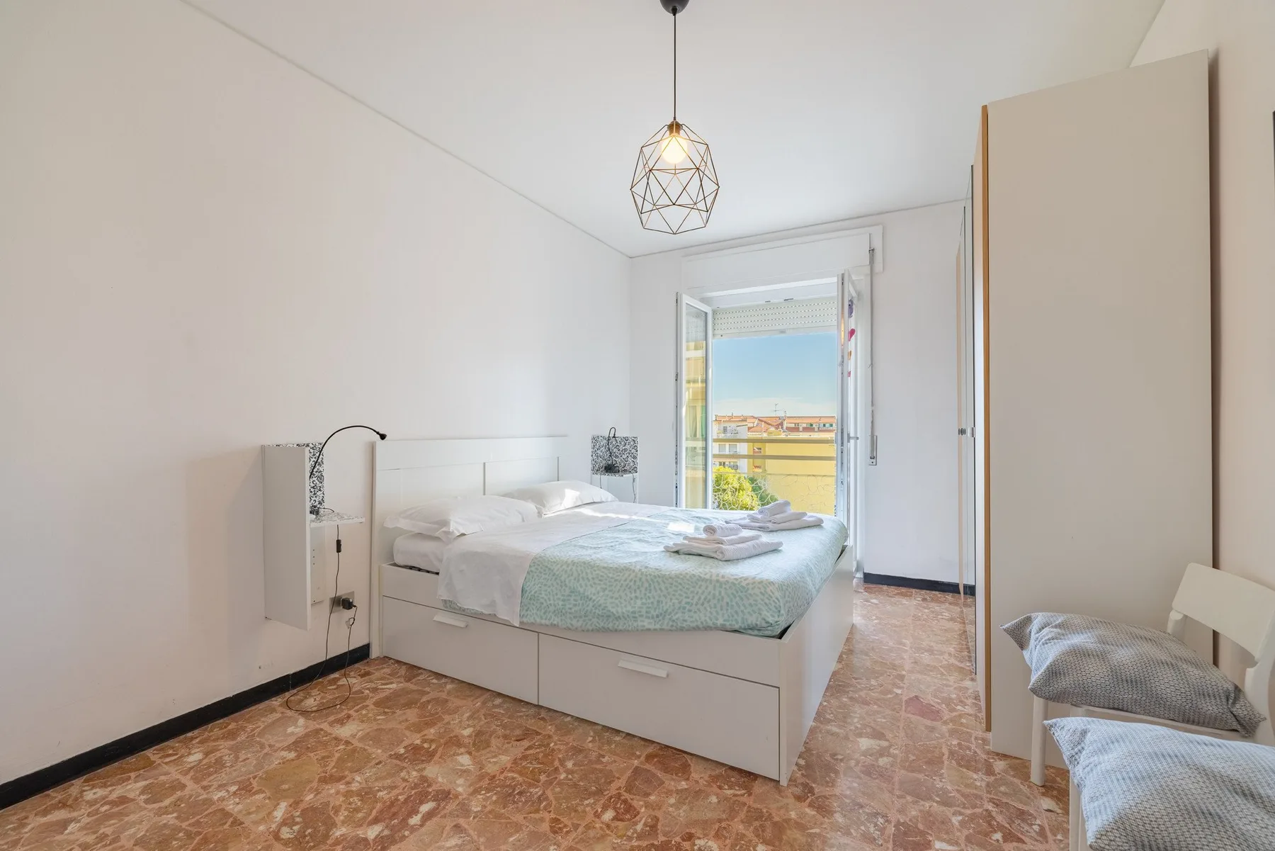 Un dormitorio luminoso con una cama bien hecha junto a una ventana amplia.