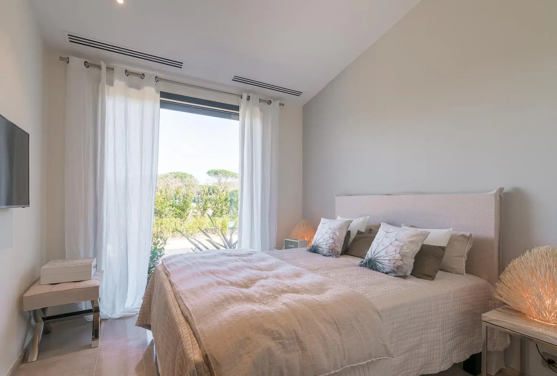 Cama doble blanca con una puerta corredera de cristal que da al exterior