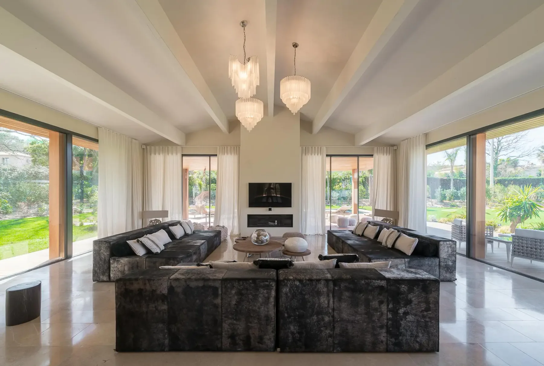 Sala de estar con grandes sofás oscuros, una mesa entre ellos y lámparas colgantes