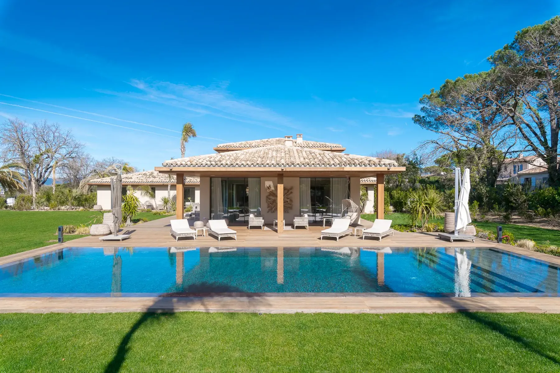 Gran piscina rodeada de césped, con una amplia terraza detrás