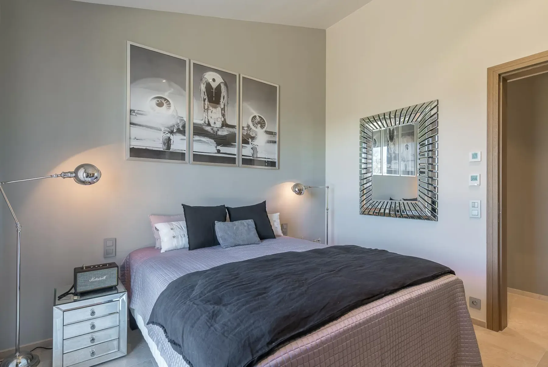 Dormitorio con cama doble, una obra de arte encima y un espejo colgado a la derecha de la imagen