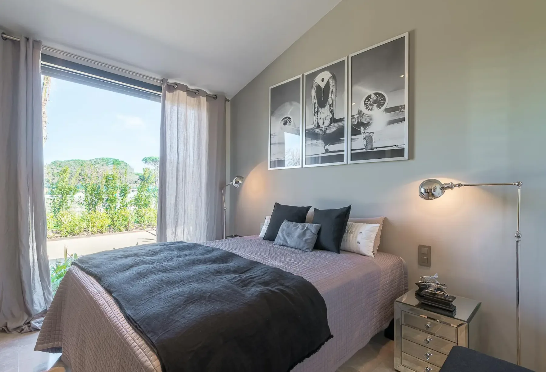 Cama doble con una obra de arte en la pared encima y una puerta corredera de cristal que da al exterior