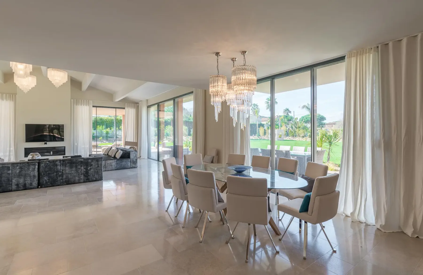 Comedor con mesa, sillas y lámparas colgantes, con la sala de estar al fondo
