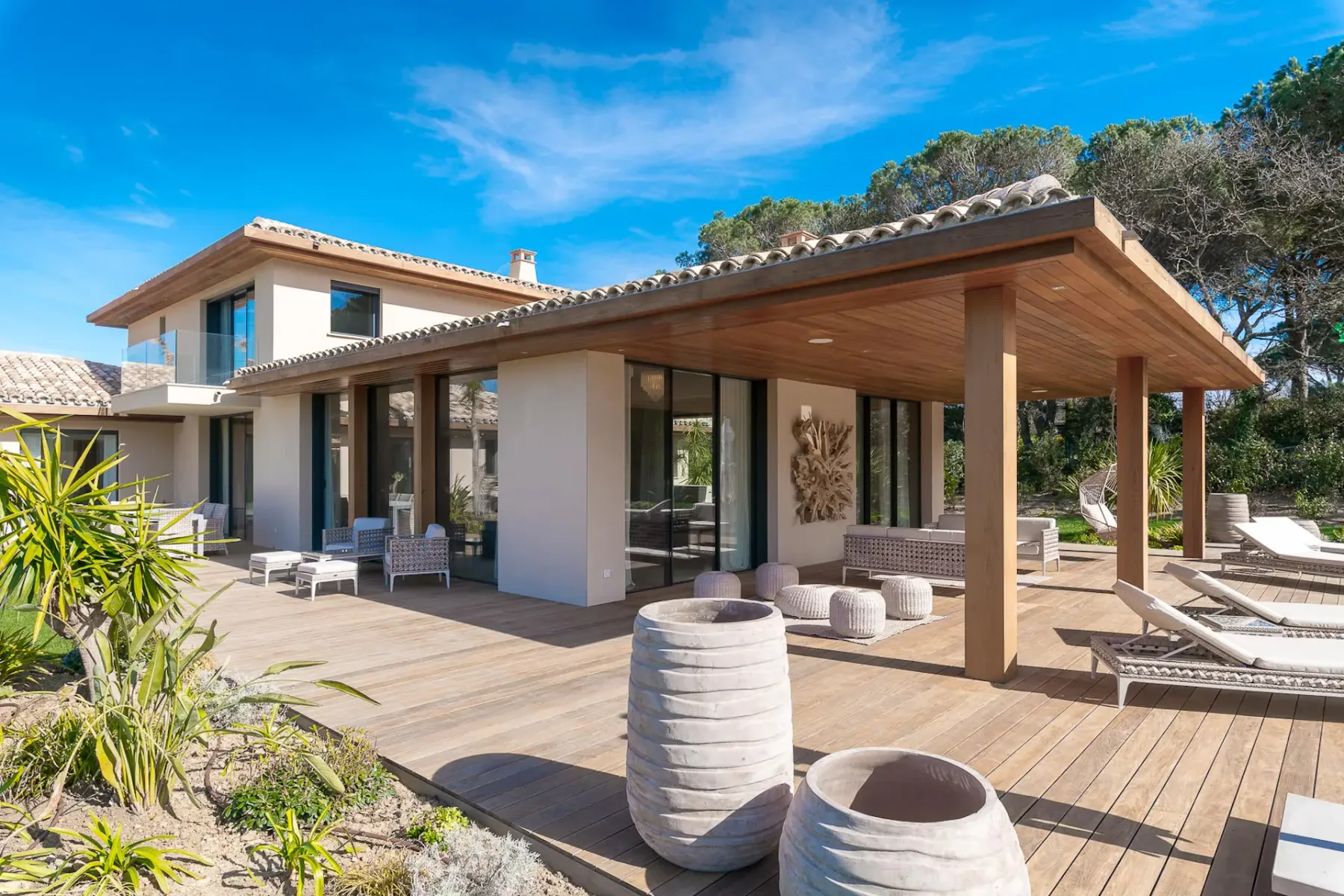 Una casa moderna se abre a una terraza de madera con asientos y tumbonas.