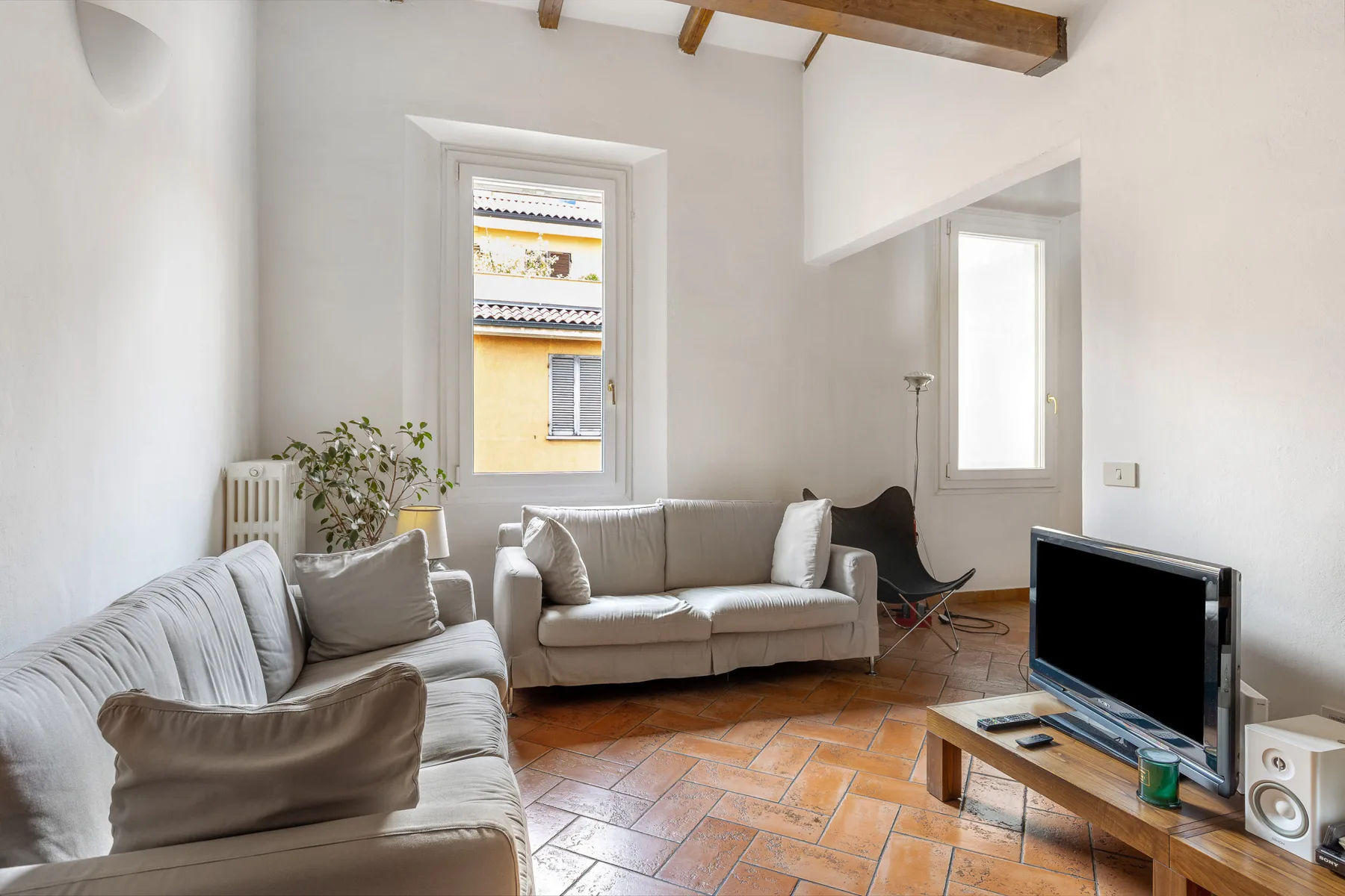 A bright living room with seating, a television, and exposed ceiling beams.