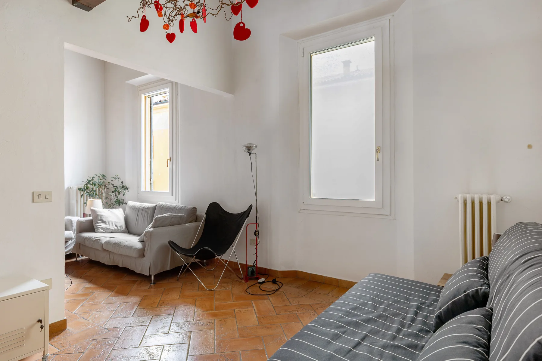 A bright living room with seating, a large window, and patterned tile flooring.