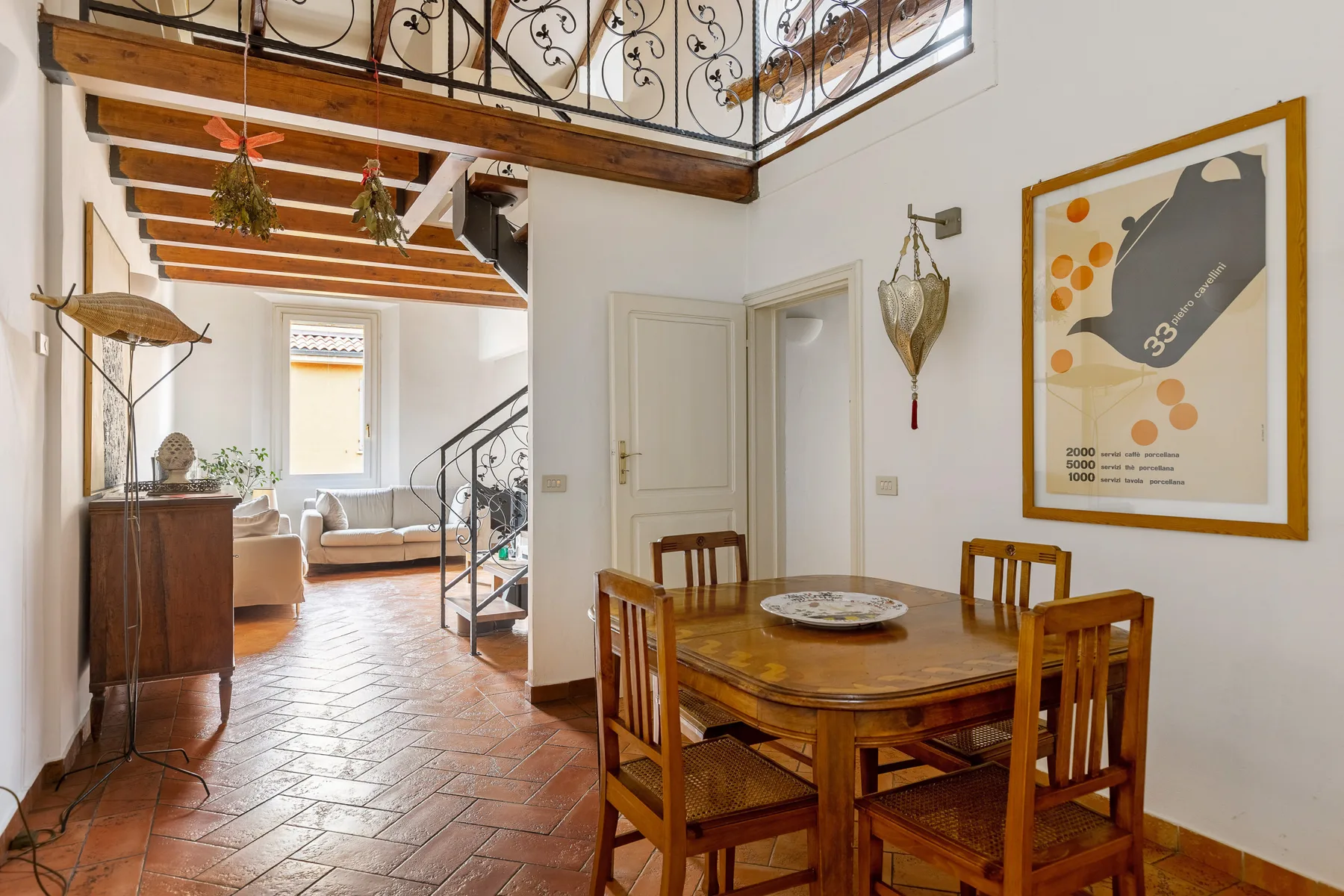 A dining area with a wooden table and chairs beneath an upstairs railing.