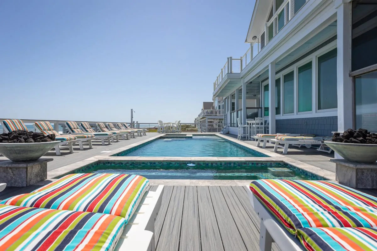 Una piscina en la azotea junto a un edificio moderno, con cojines a rayas en primer plano.