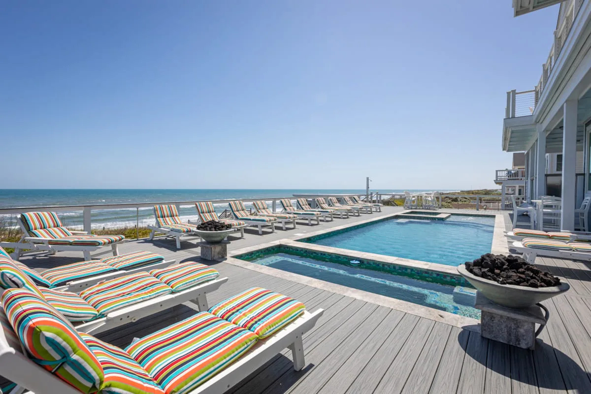Una terraza junto al mar con piscina, tumbonas a rayas y vistas al océano.