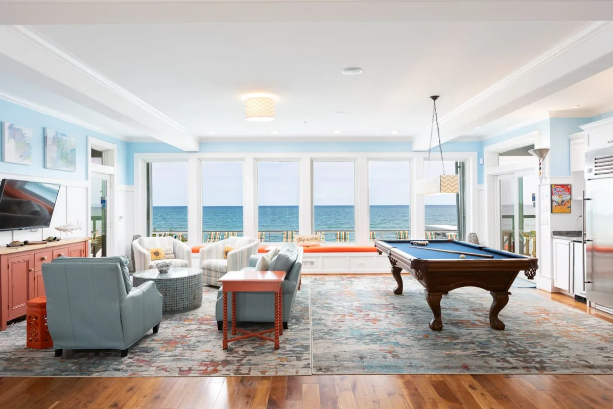 A bright living room with seating, a pool table, and ocean views through large windows.