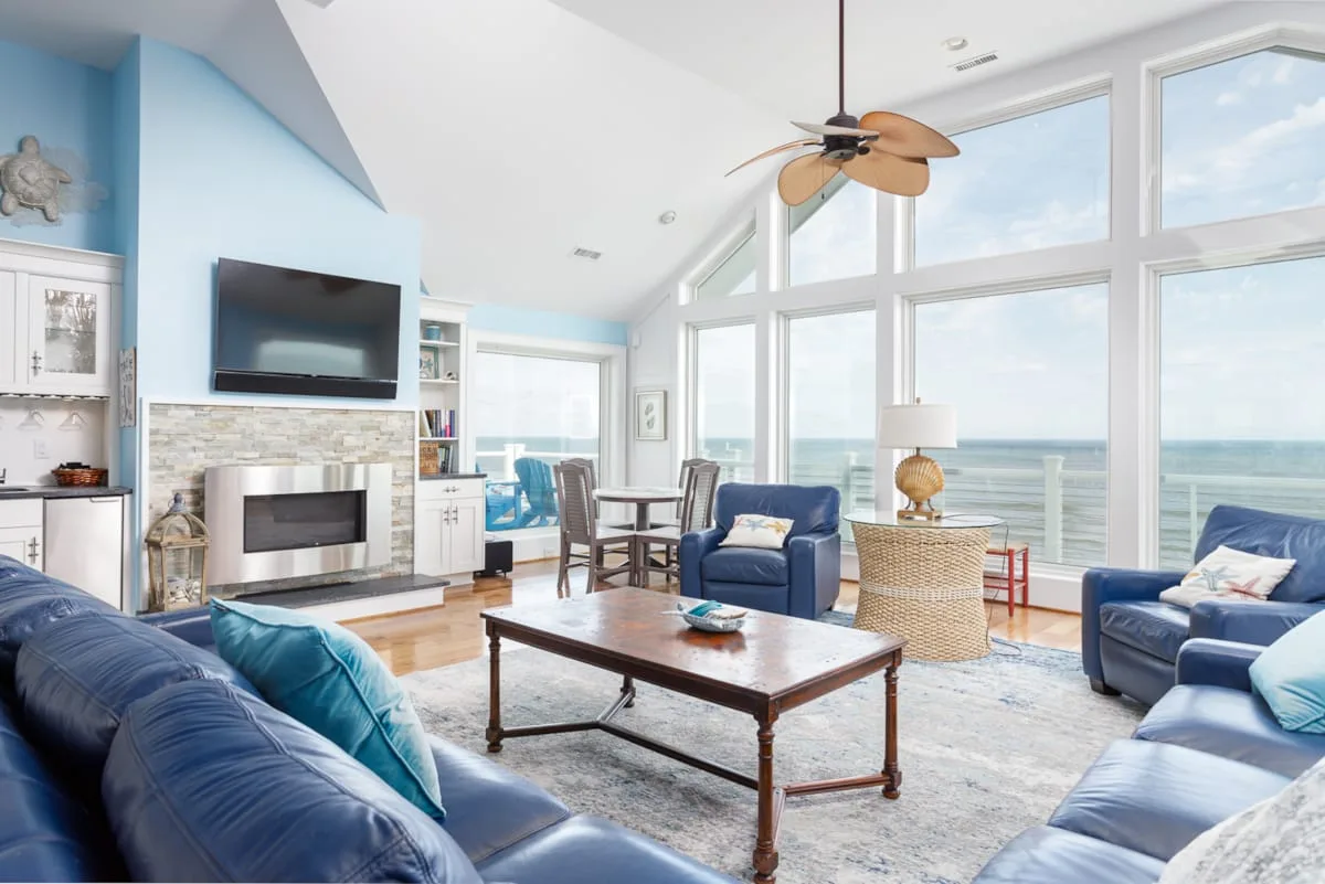 A bright living room with blue seating and large windows overlooking the water.