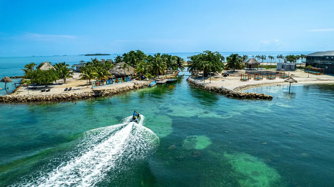 A speedboat crossing turquoise water toward tropical islands.