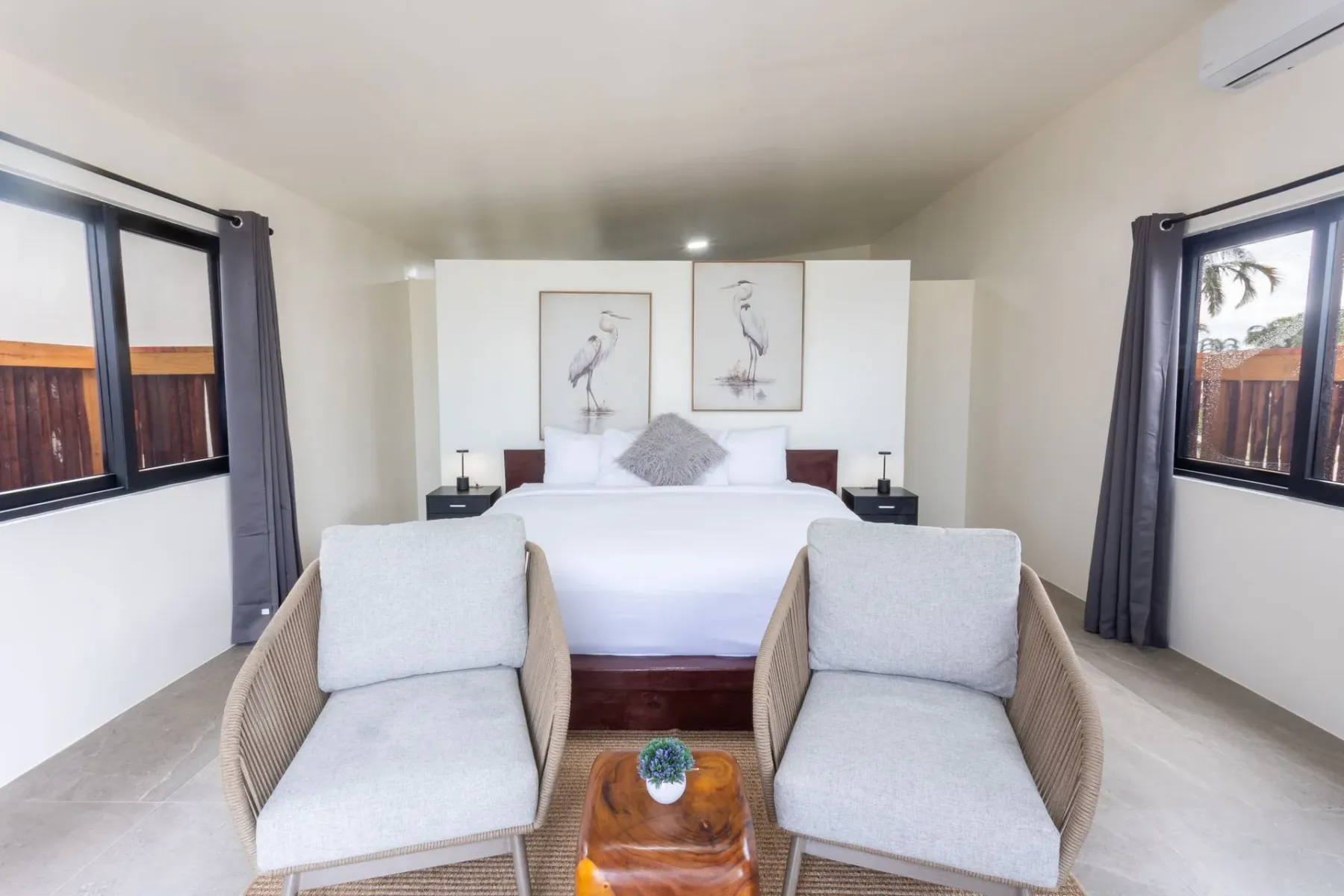 Bedroom with a white bed, wicker chairs, and large windows.