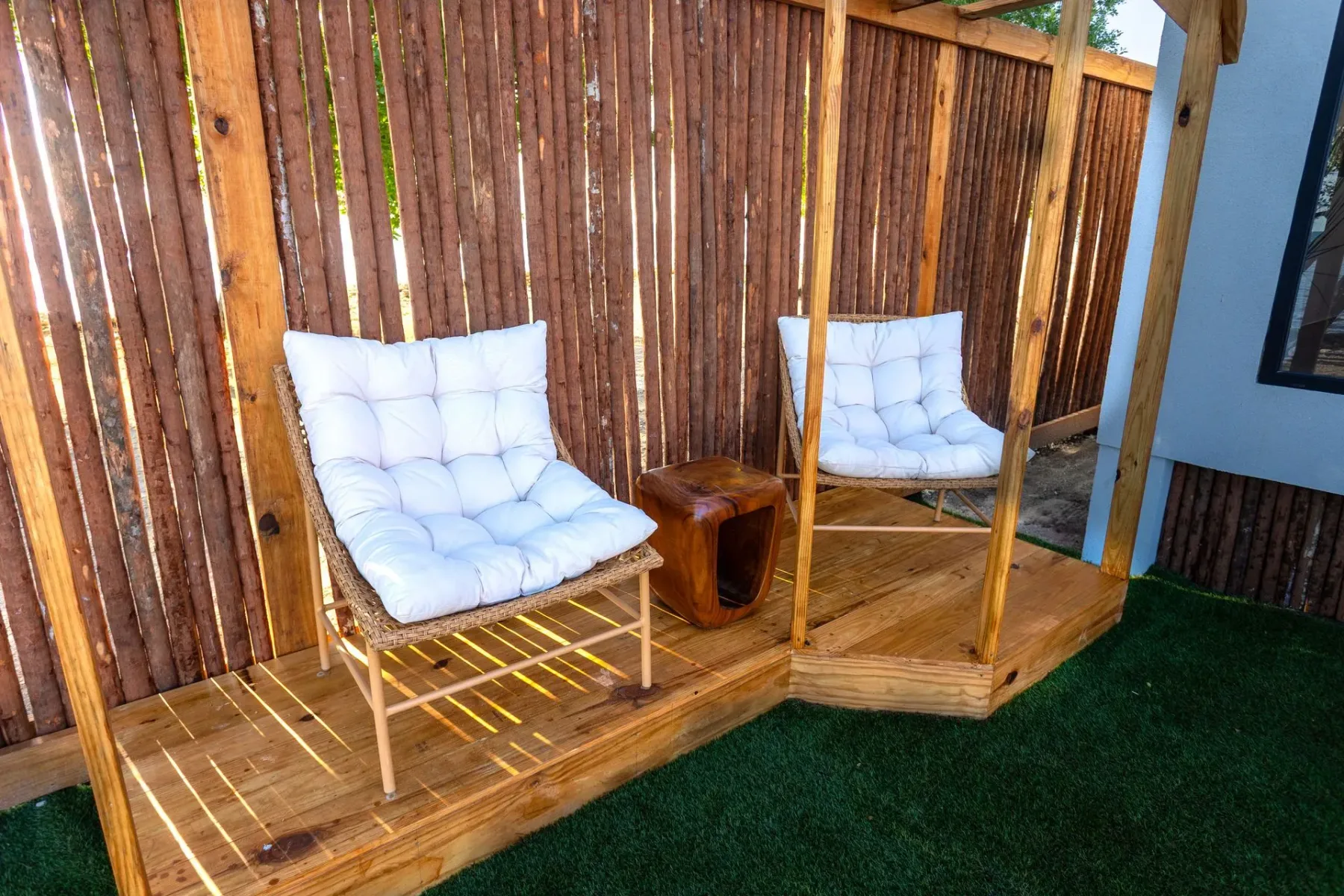 Two cushioned chairs on a deck beside a bamboo fence.