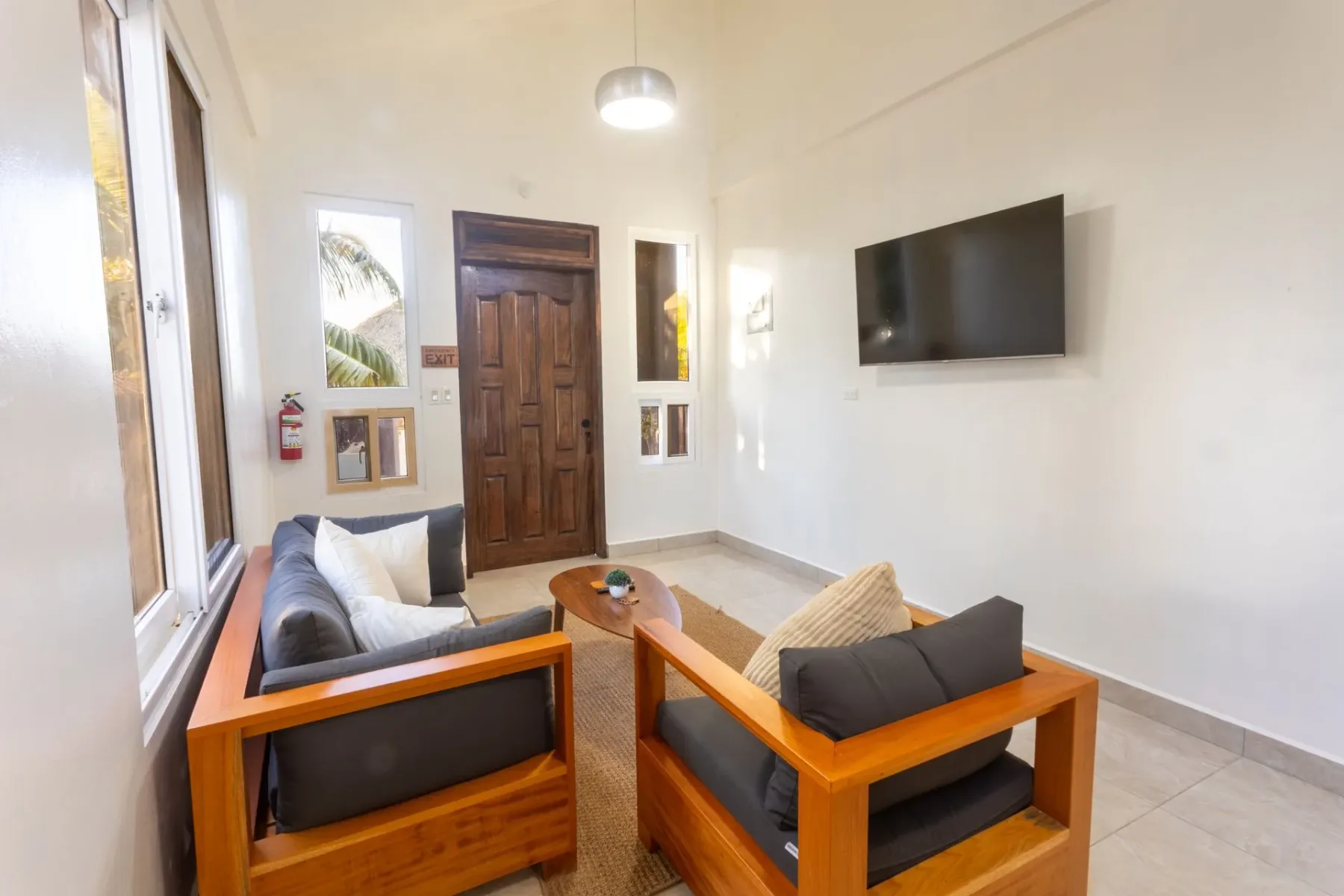 Living room with wooden sofas, a wall-mounted TV, and large windows.
