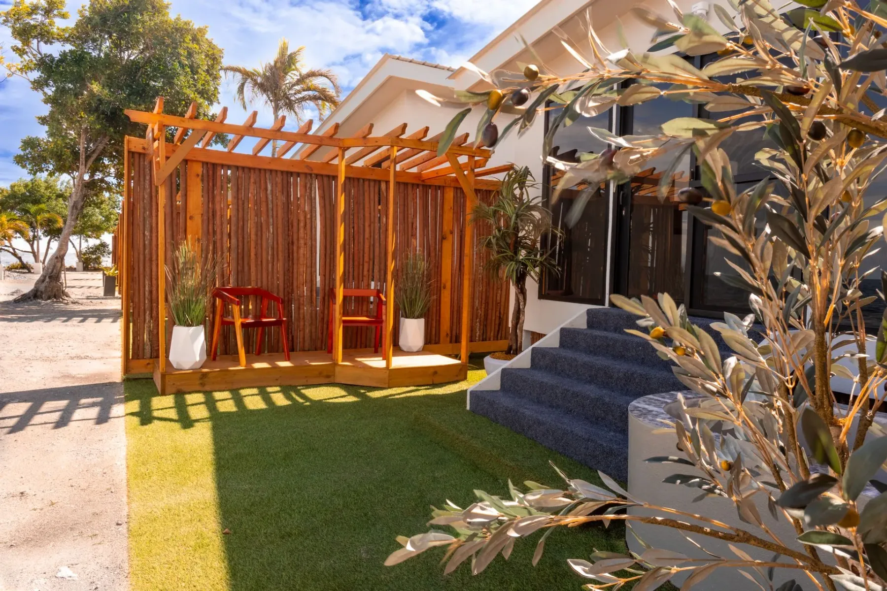 Patio with a wooden pergola, chairs, steps, and landscaped lawn.