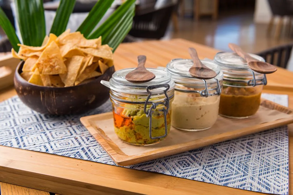 Una presentación sobre la mesa con frascos de salsas y un cuenco de chips.