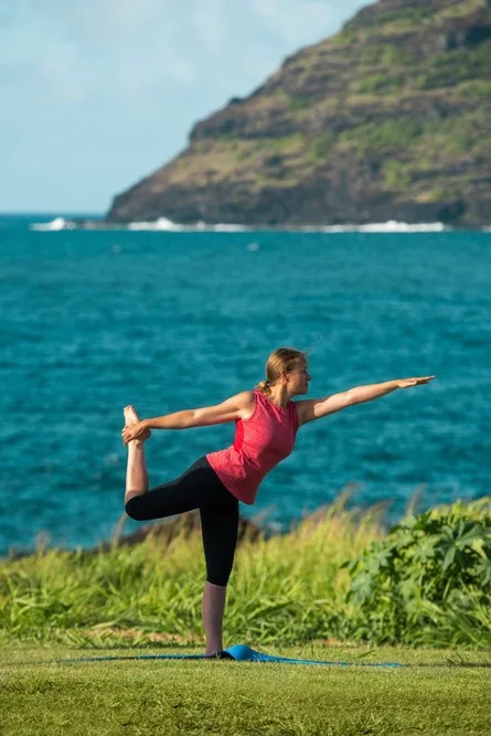 Una persona practica una postura de equilibrio de yoga sobre una esterilla junto al mar.