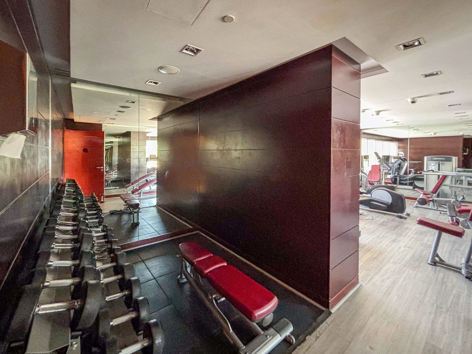 Un gimnasio con pesas, bancos rojos y máquinas de ejercicio.