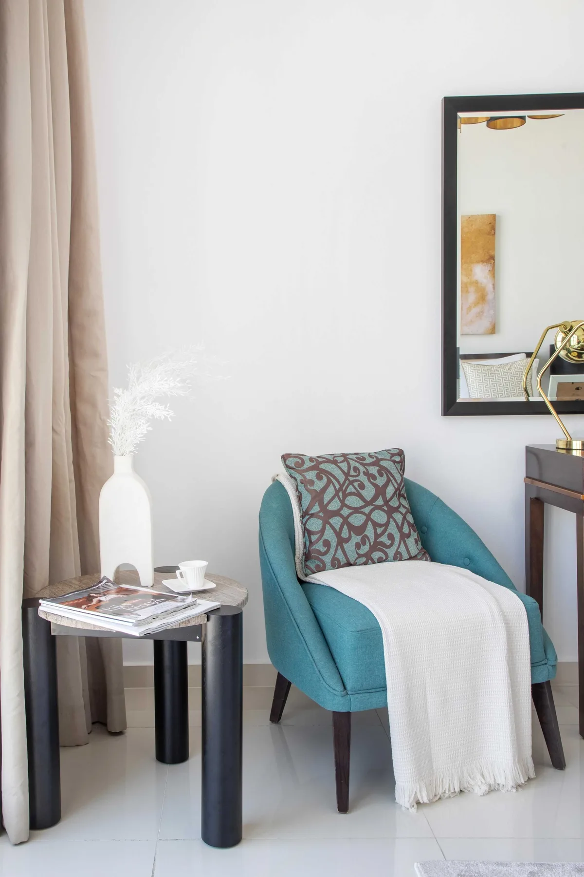 Una zona de estar luminosa con un sillón turquesa, una mesa auxiliar y un espejo.