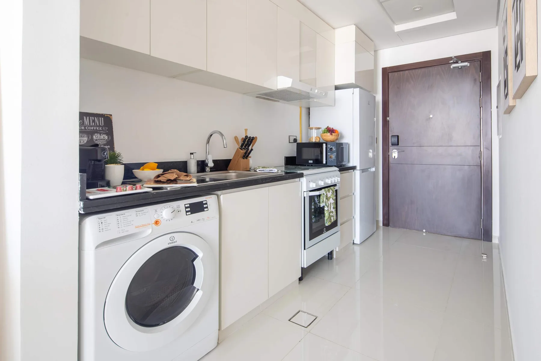 Una cocina compacta con armarios blancos, una lavadora y electrodomésticos de cocina.