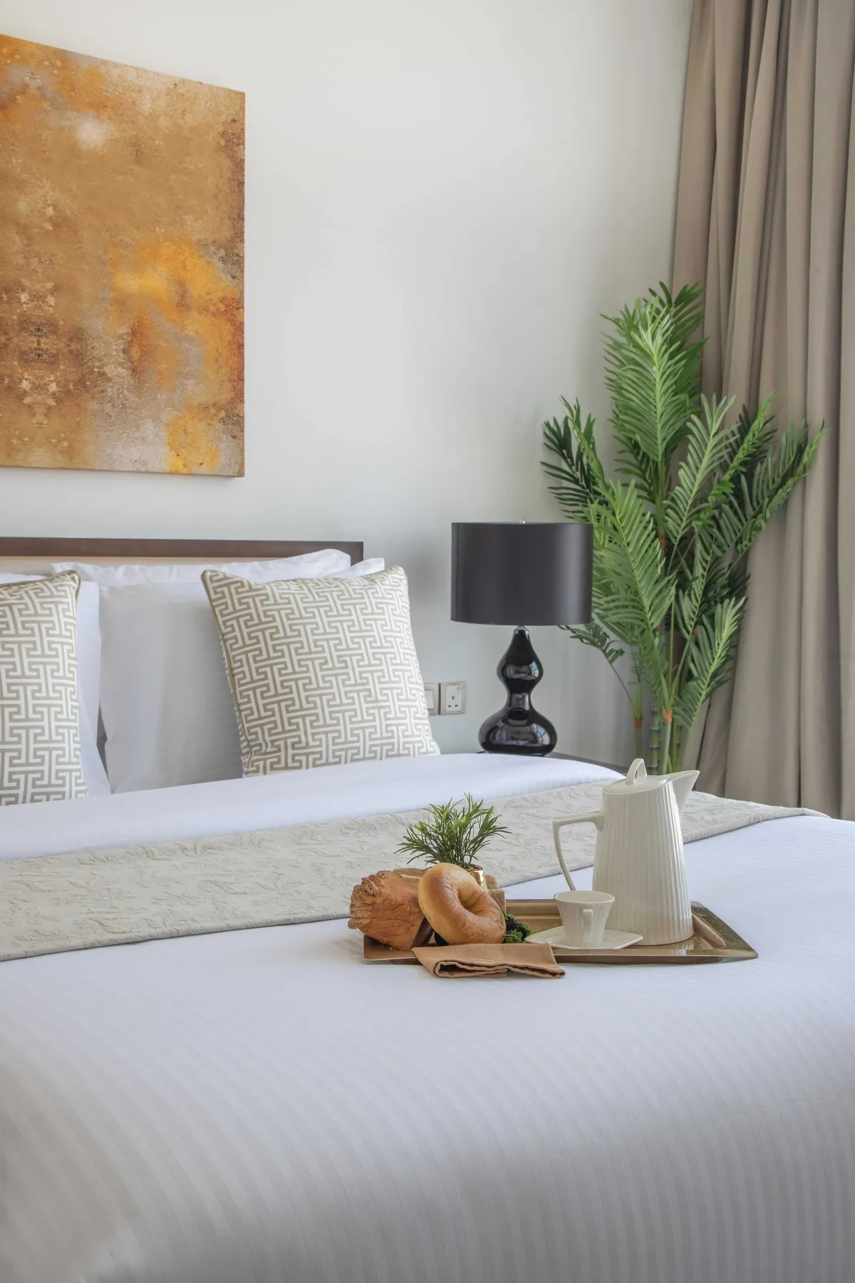 Un dormitorio ordenado con cojines estampados, una lámpara de noche y una planta frondosa.