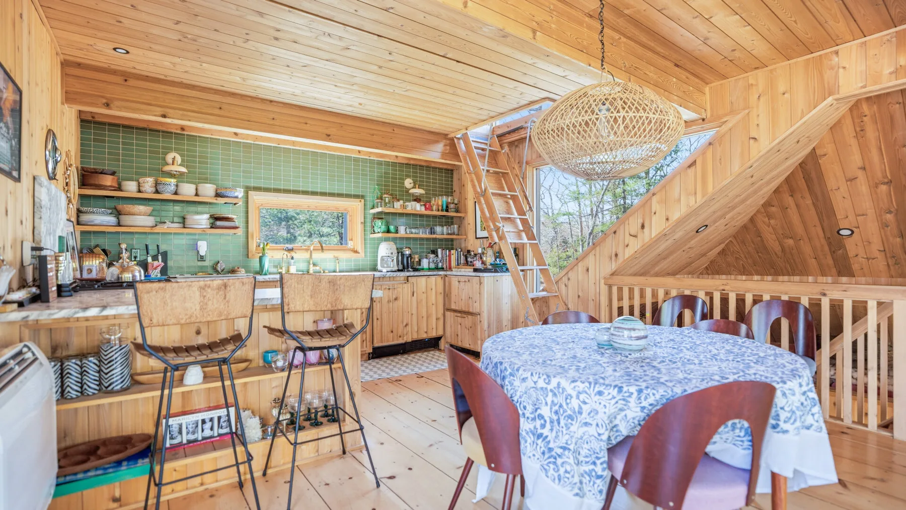 Una cocina y comedor revestidos de madera, con una mesa y asientos junto a la barra.