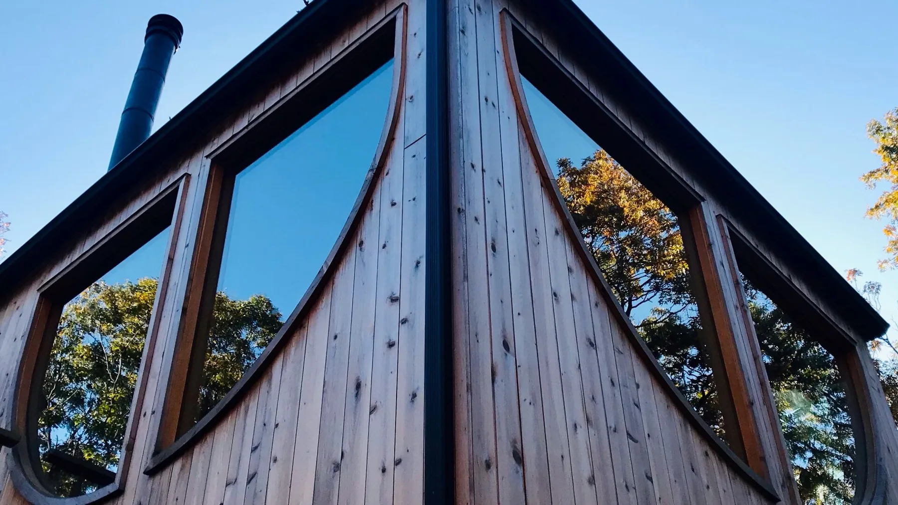 Exterior de madera con ventanas altas que reflejan los árboles cercanos.