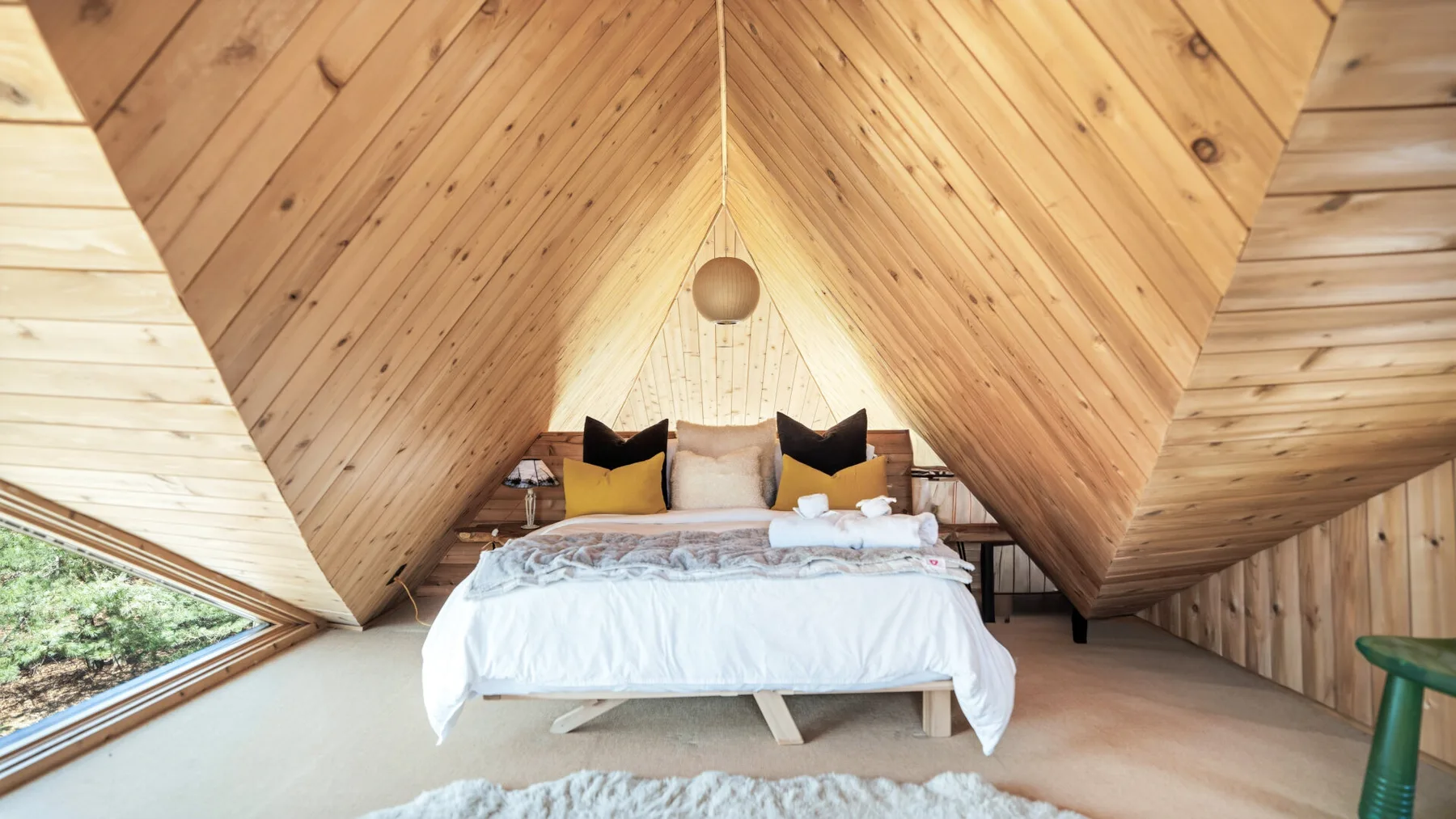 Un dormitorio con una cama bajo un techo inclinado de madera y una lámpara colgante.