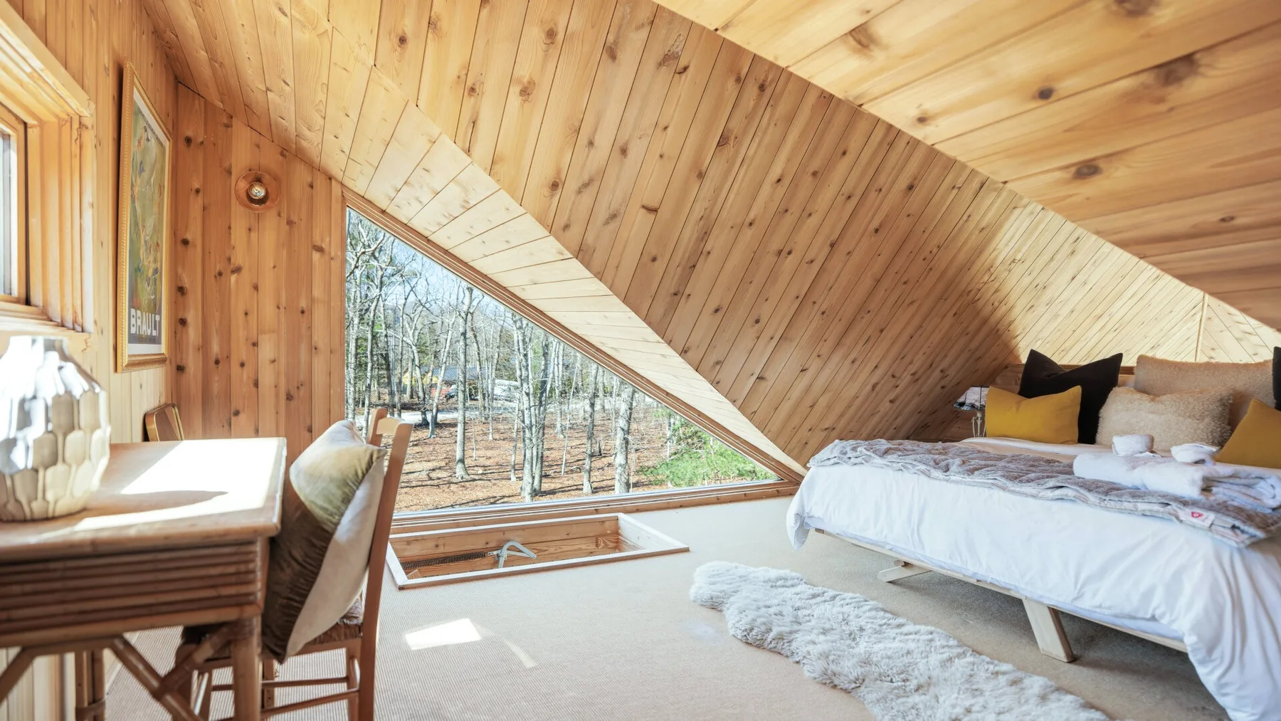 Un dormitorio revestido de madera con una cama junto a una gran ventana inclinada.