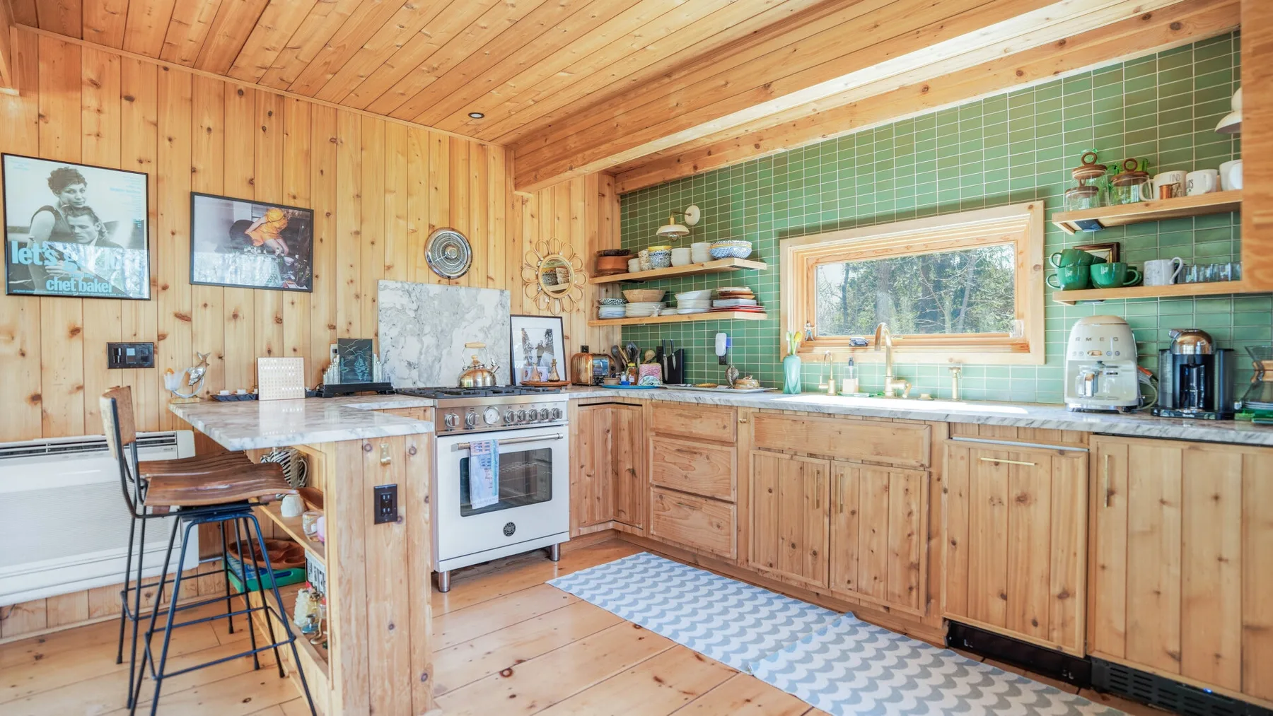 Una cocina revestida de madera con una encimera larga, azulejos verdes y una ventana sobre el fregadero.