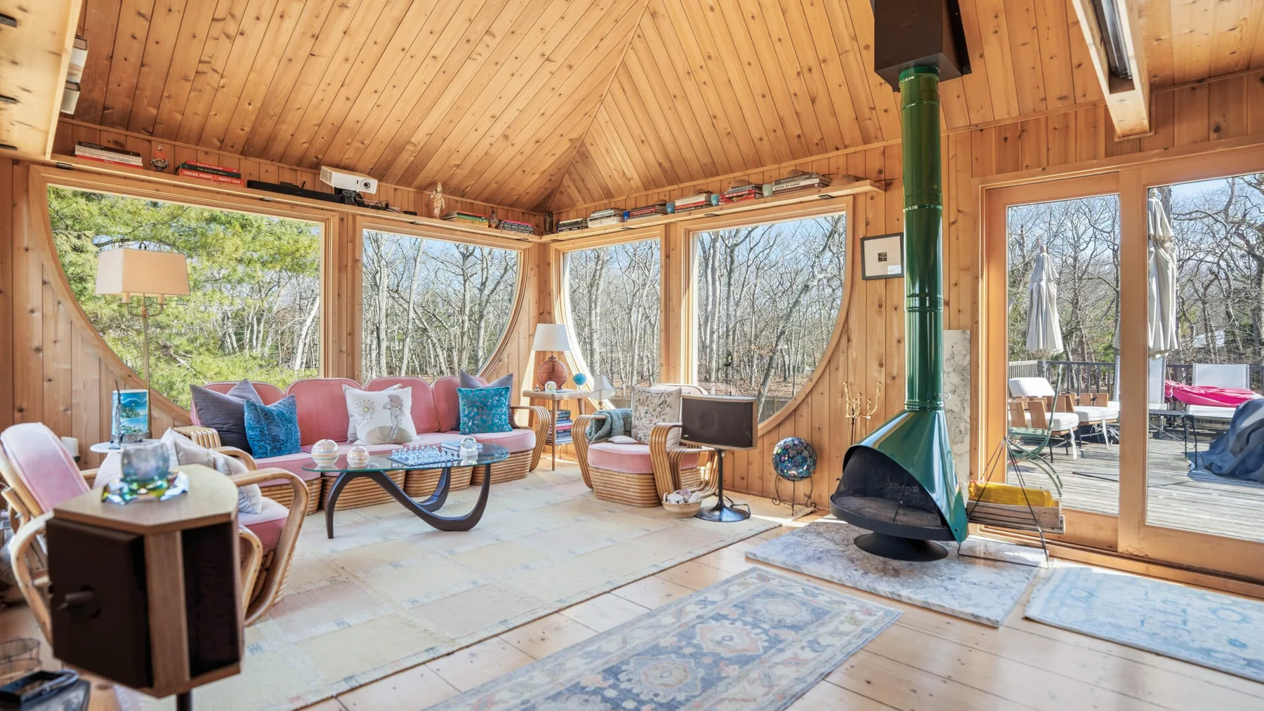 Sala de estar revestida de madera, con grandes ventanas y una estufa independiente.