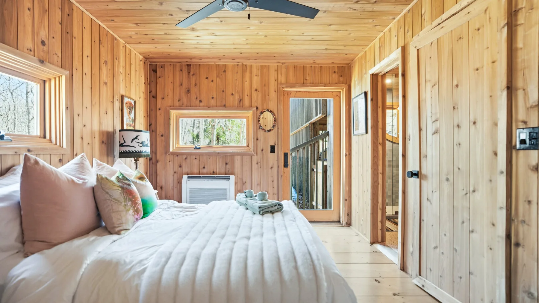 Dormitorio revestido de madera con una cama, ventanas y una puerta de vidrio.