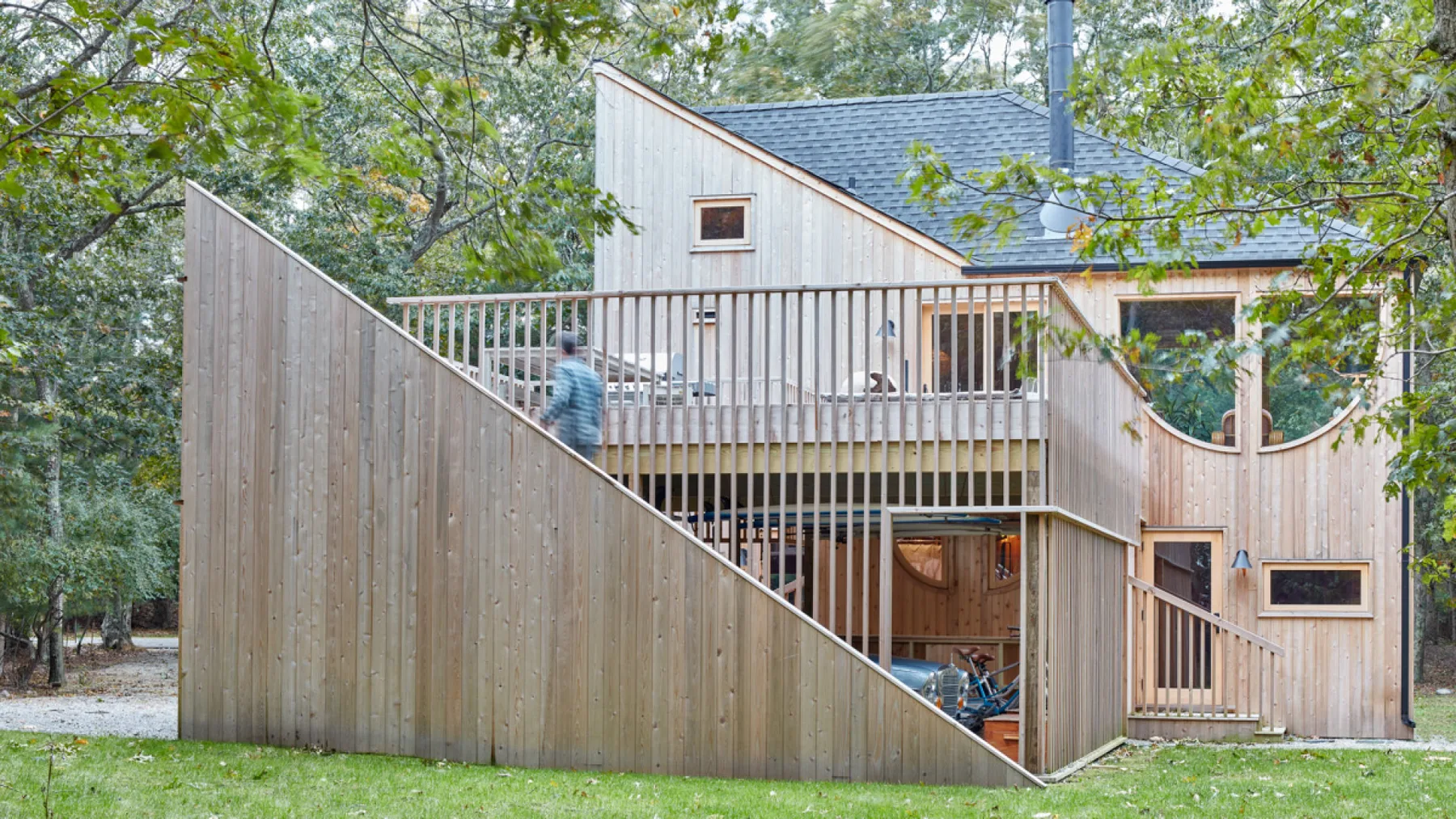 Una casa de madera con una terraza elevada y escaleras exteriores está entre los árboles.
