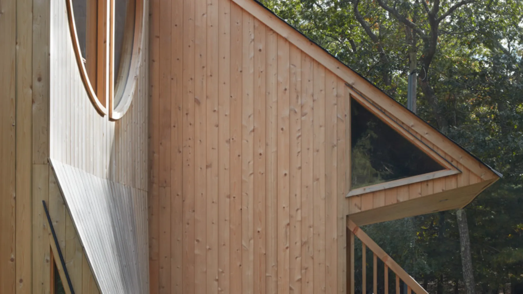 Exterior de un edificio de madera con una ventana triangular y árboles alrededor.