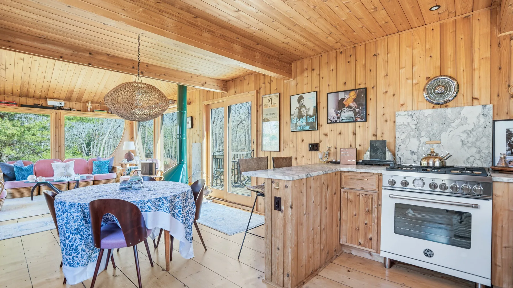 Cocina y comedor revestidos de madera, con una mesa junto a grandes ventanas.