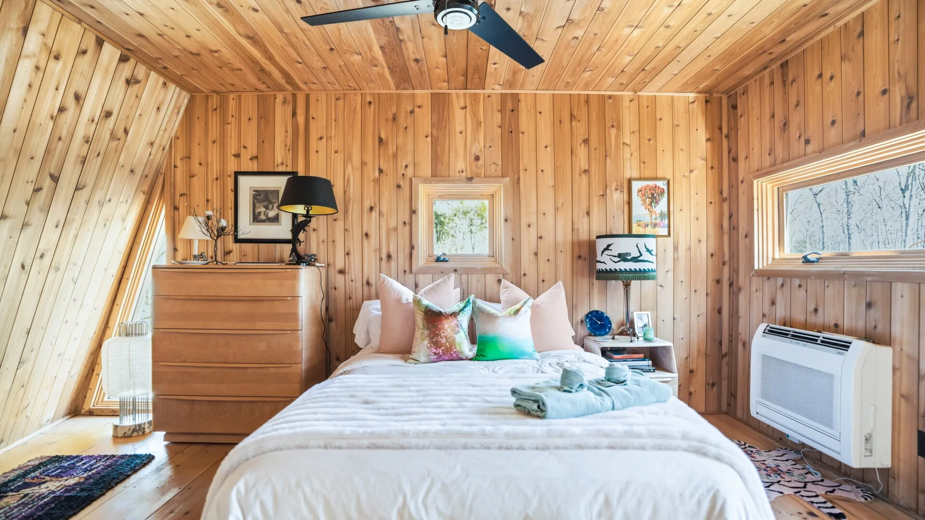 Un dormitorio revestido de madera con una cama bajo una ventana pequeña.