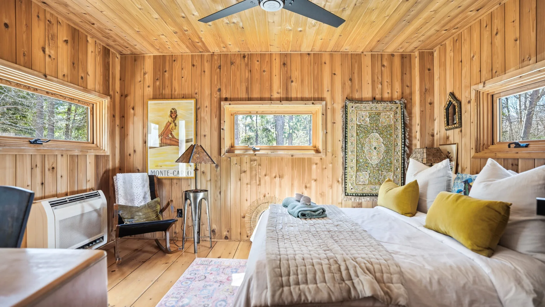 Un dormitorio revestido de madera con cama, ventanas y ventilador de techo.