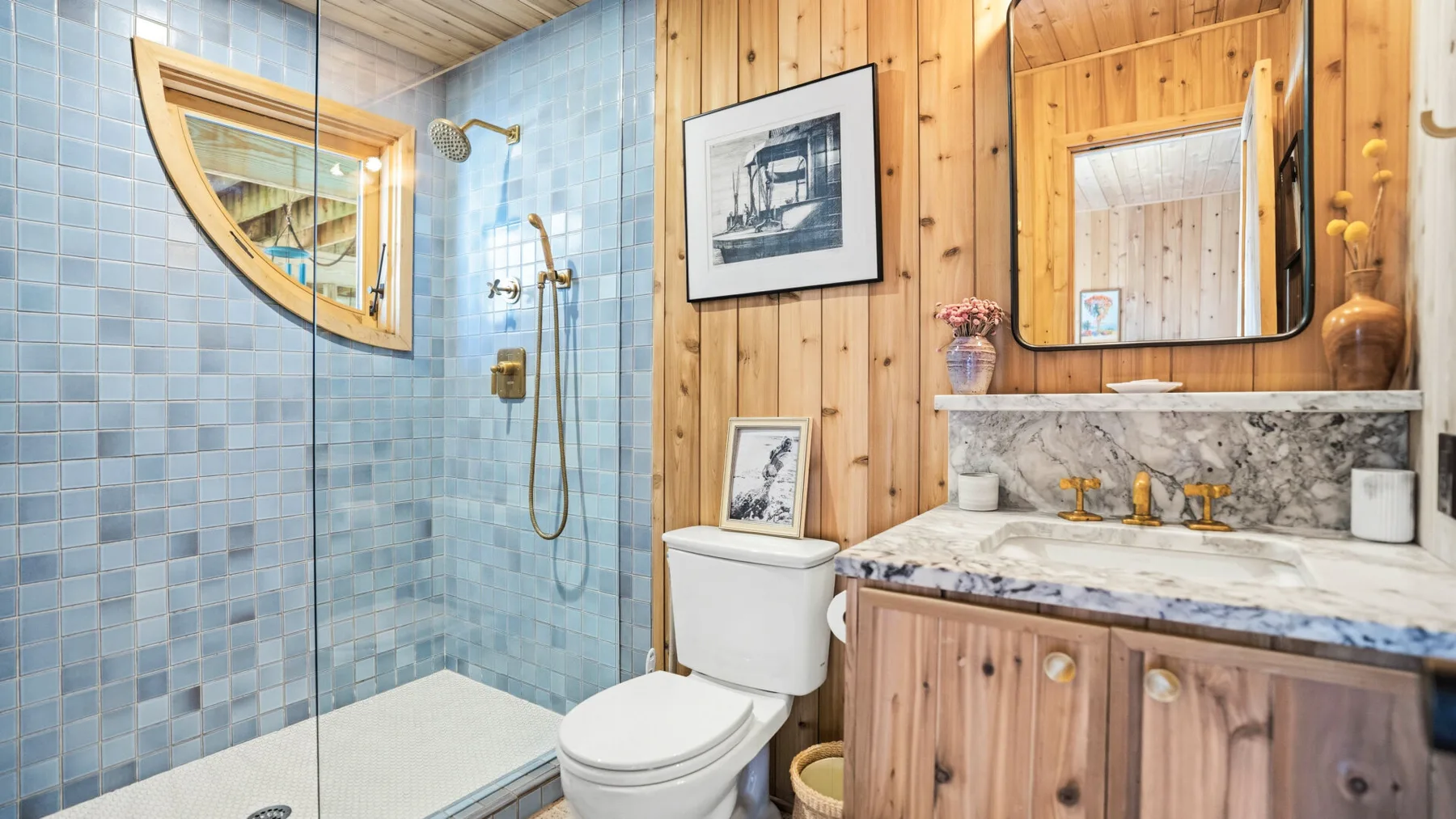 Un baño con ducha de azulejos, inodoro y tocador de madera bajo un espejo.