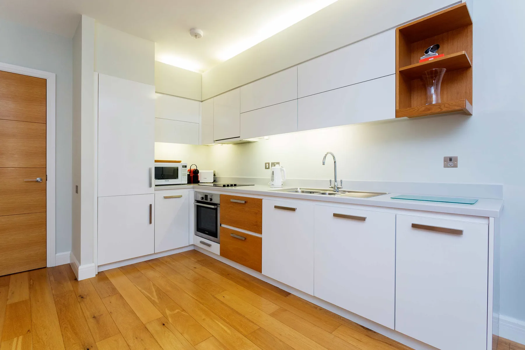 A modern kitchen with white cabinets, wood accents, and a countertop.