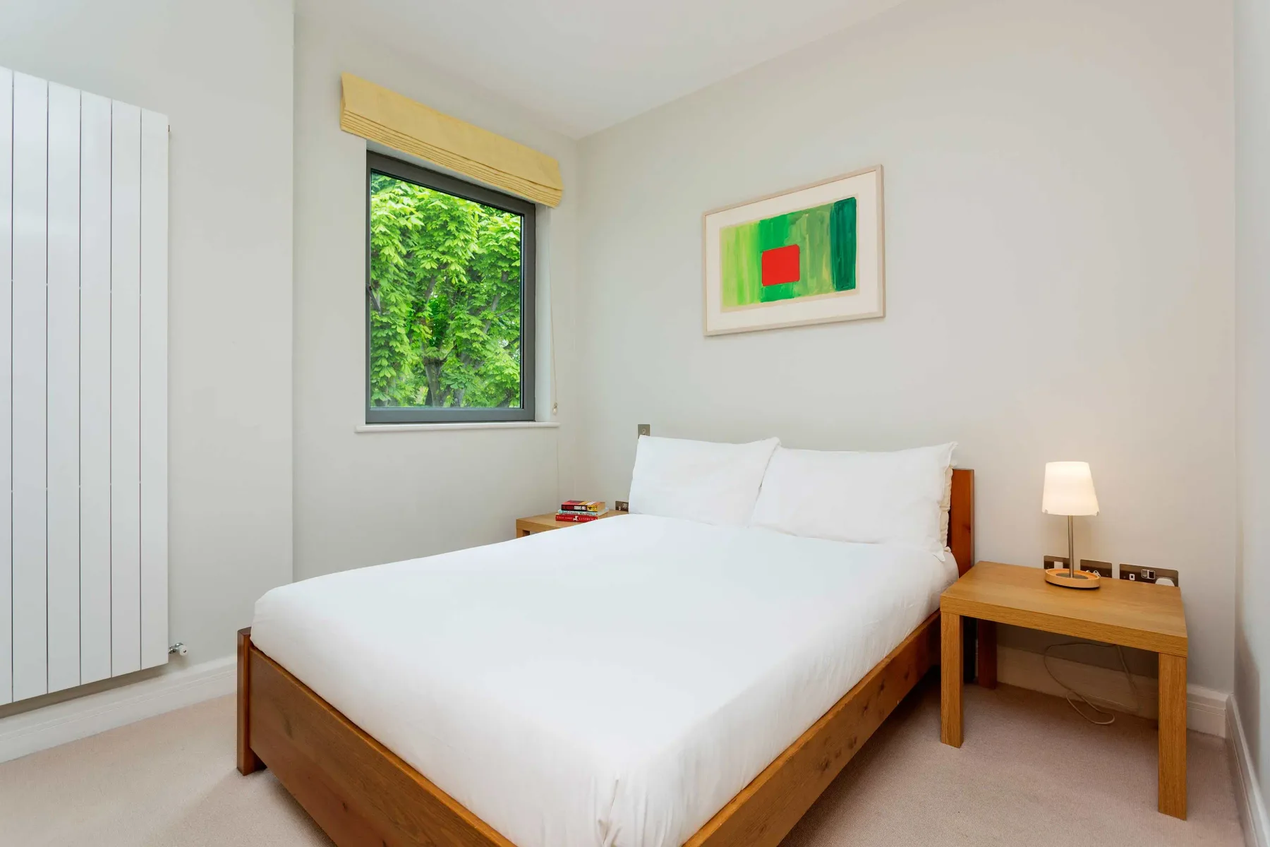 A bedroom with a wooden bed, white bedding, and a window overlooking greenery.