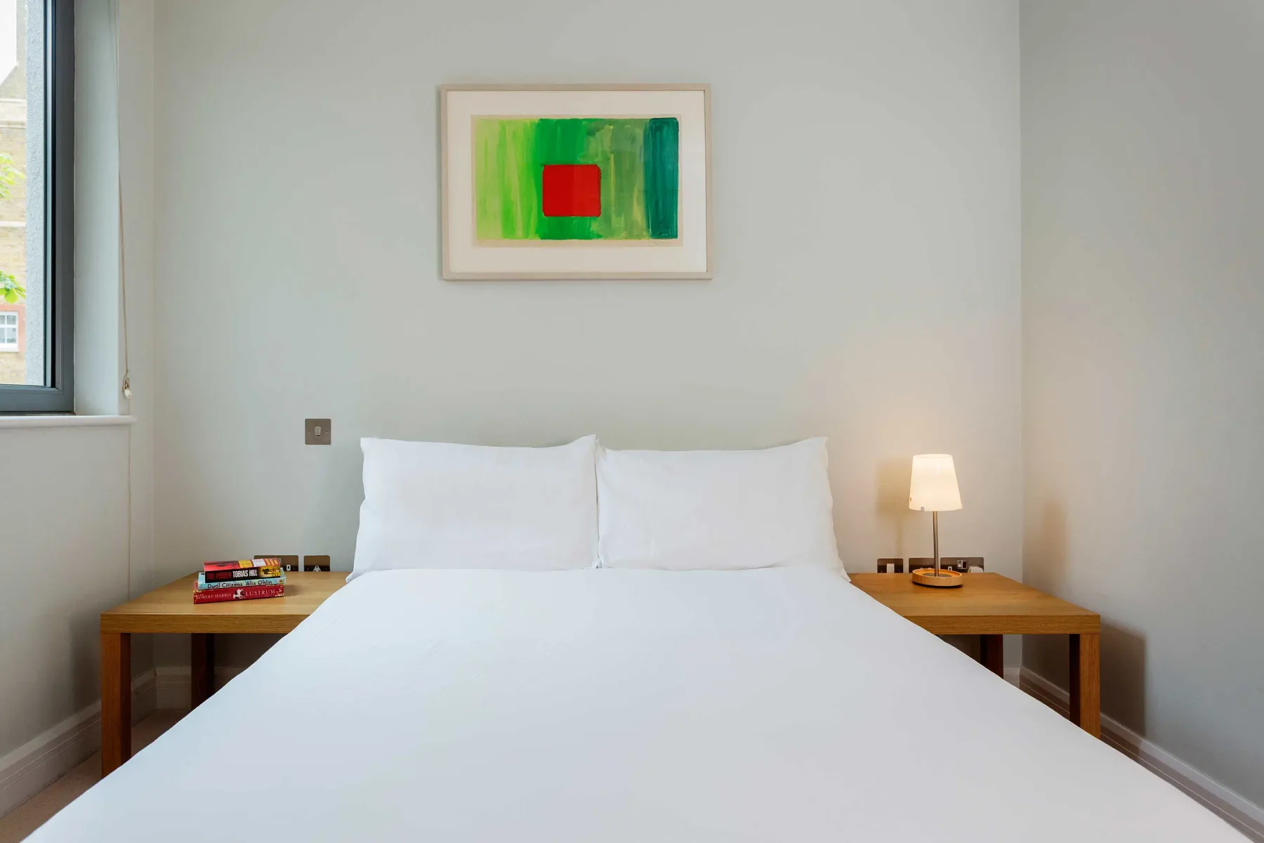 A bedroom with a neatly made bed and colorful artwork above it.