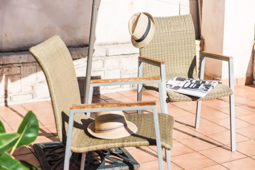 Asientos al aire libre en un patio de baldosas, con sillas tejidas y sombreros.